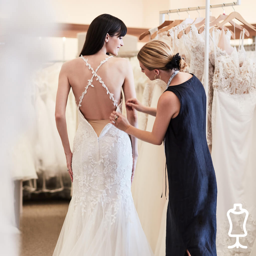 store associate helping bride with wedding dress fitting