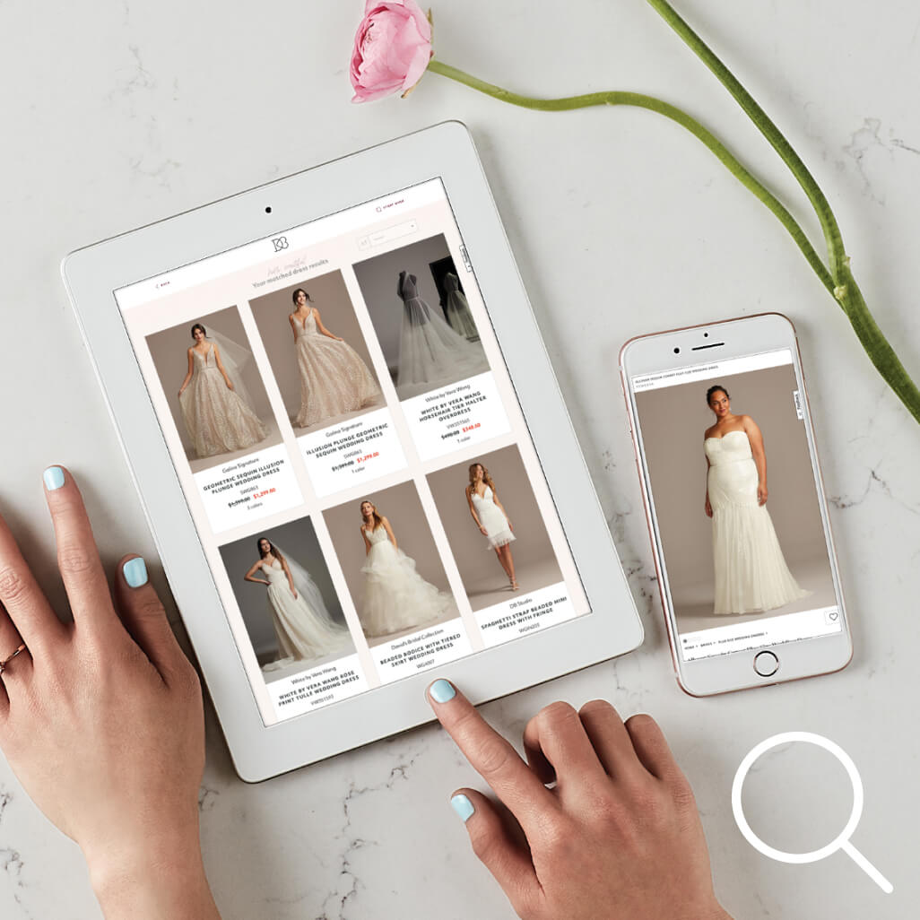 hands on an ipad showing wedding dresses next to a cell phone, and flower on a table