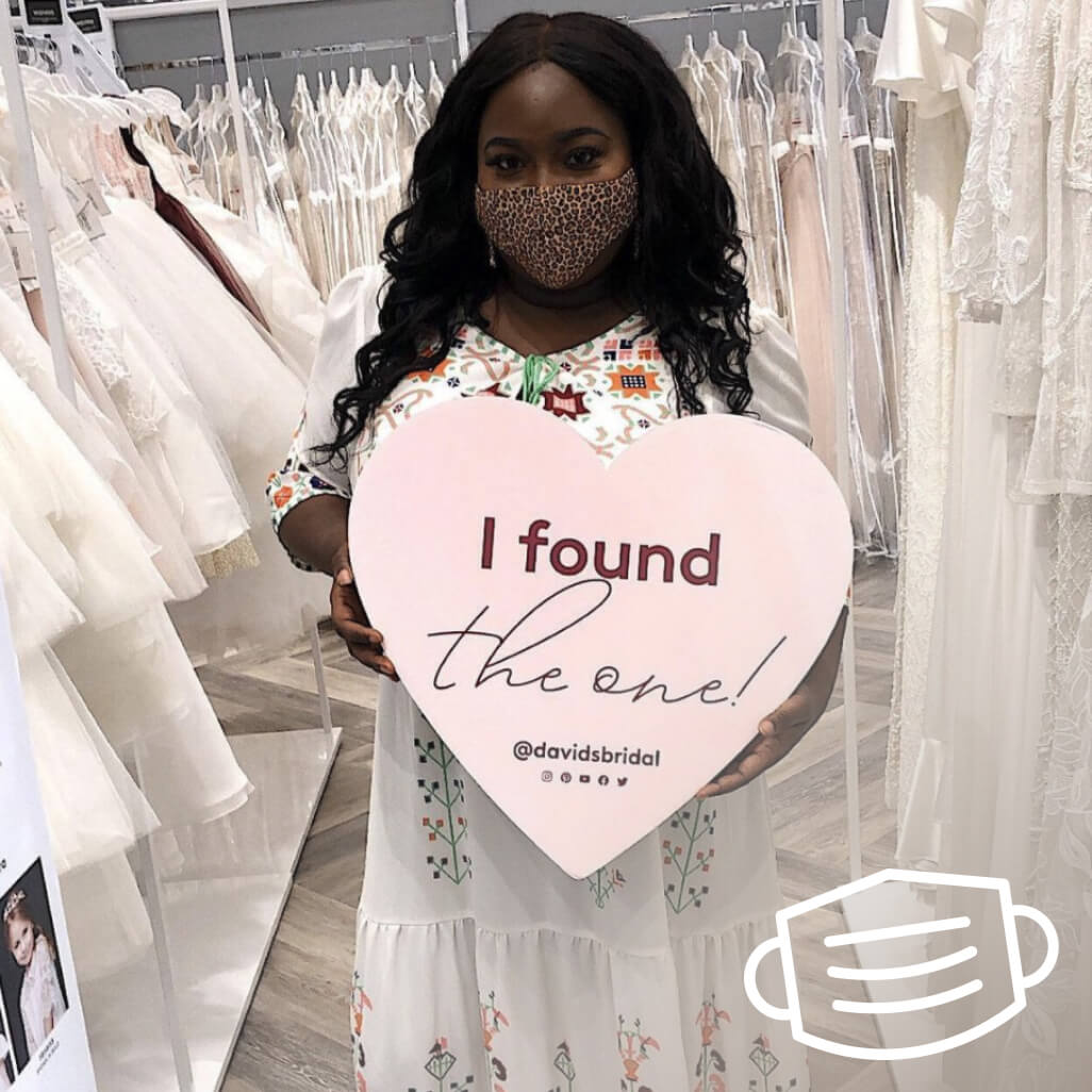 woman wearing a mask holding a heart shaped sign in a store