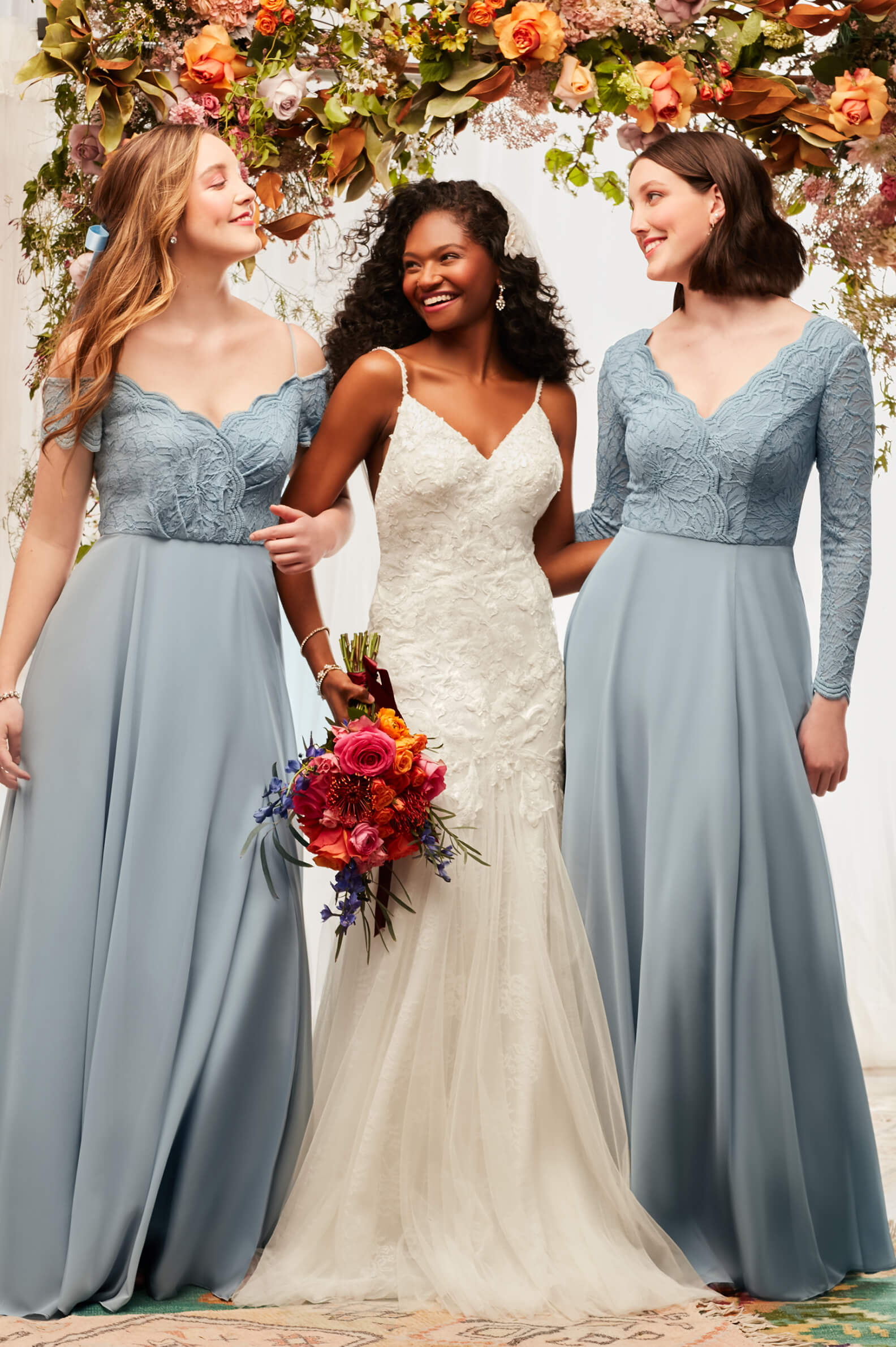 bride with her 2 bridesmaids under a flower arrangement