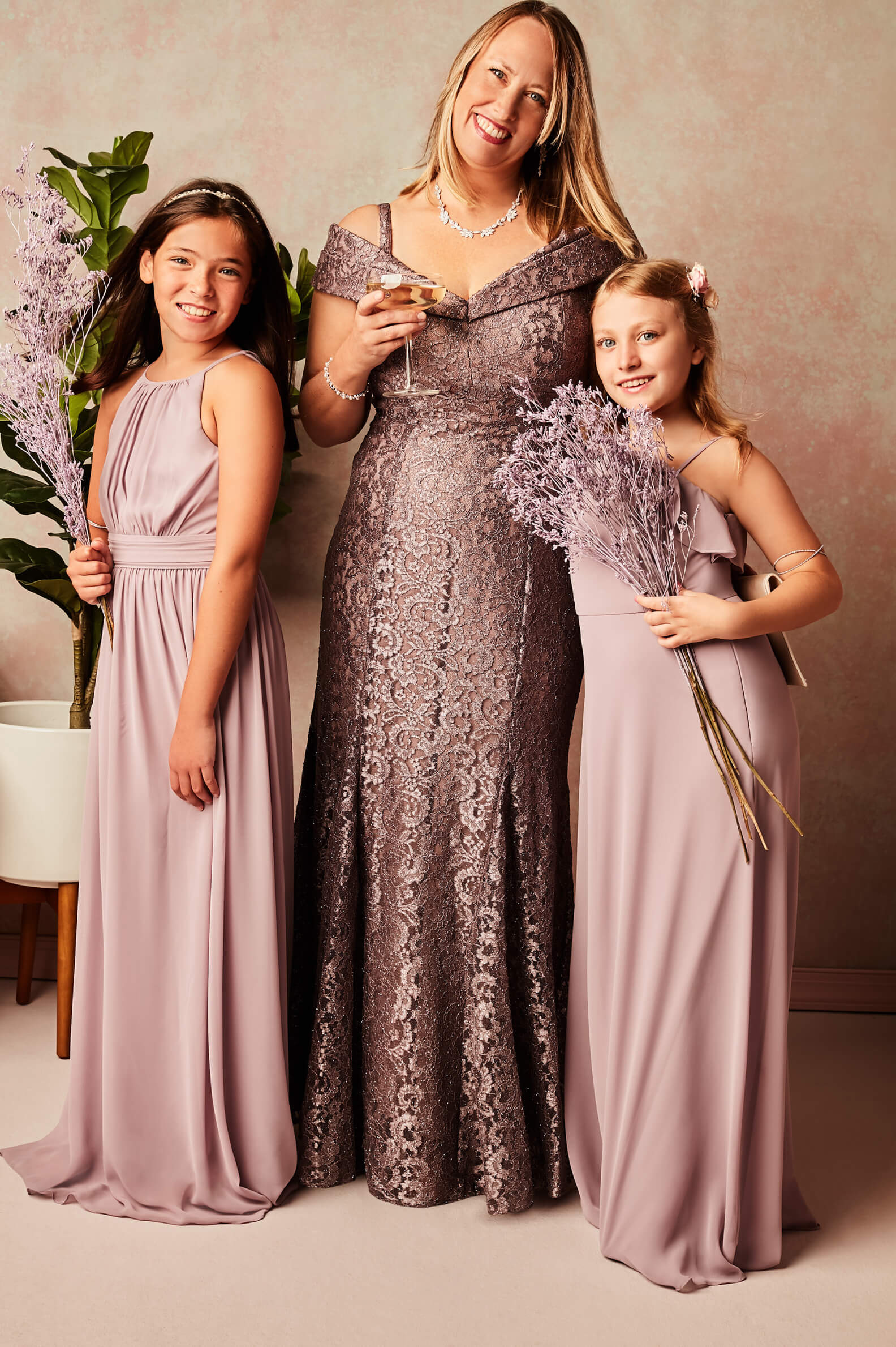 woman in off-the-shoulder dress standing with 2 girls in different gray dresses holding flowers